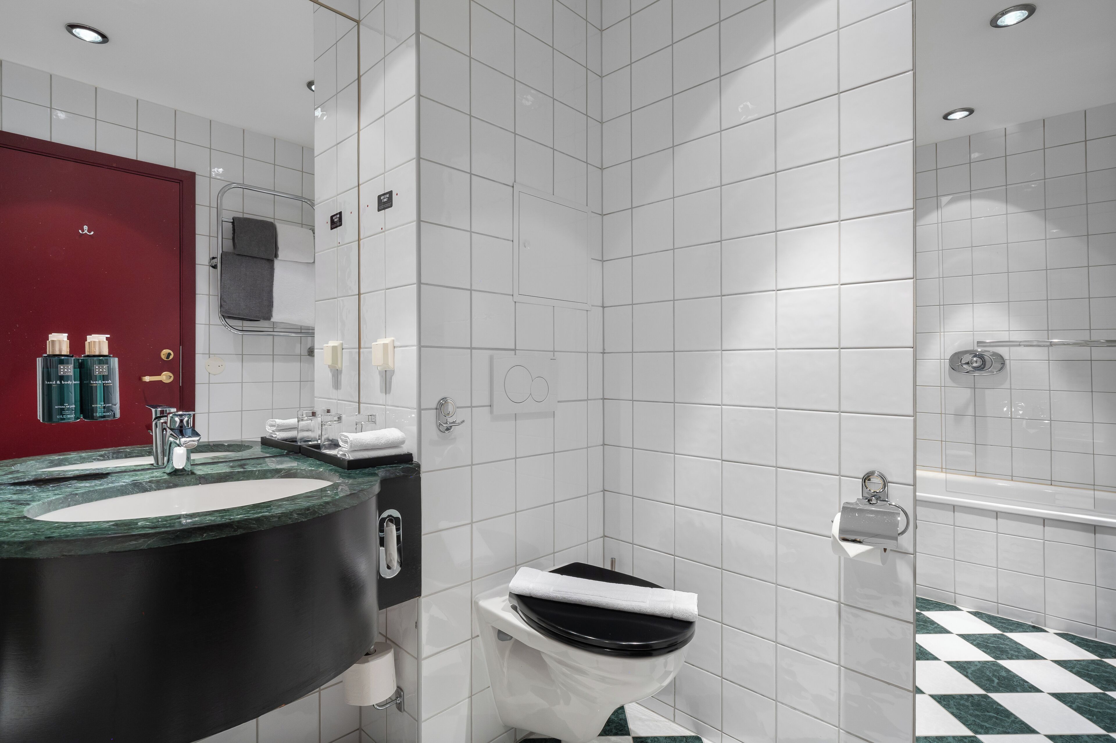 A modern bathroom with a black sink, white tiles, a red door, a shower, and a toilet.