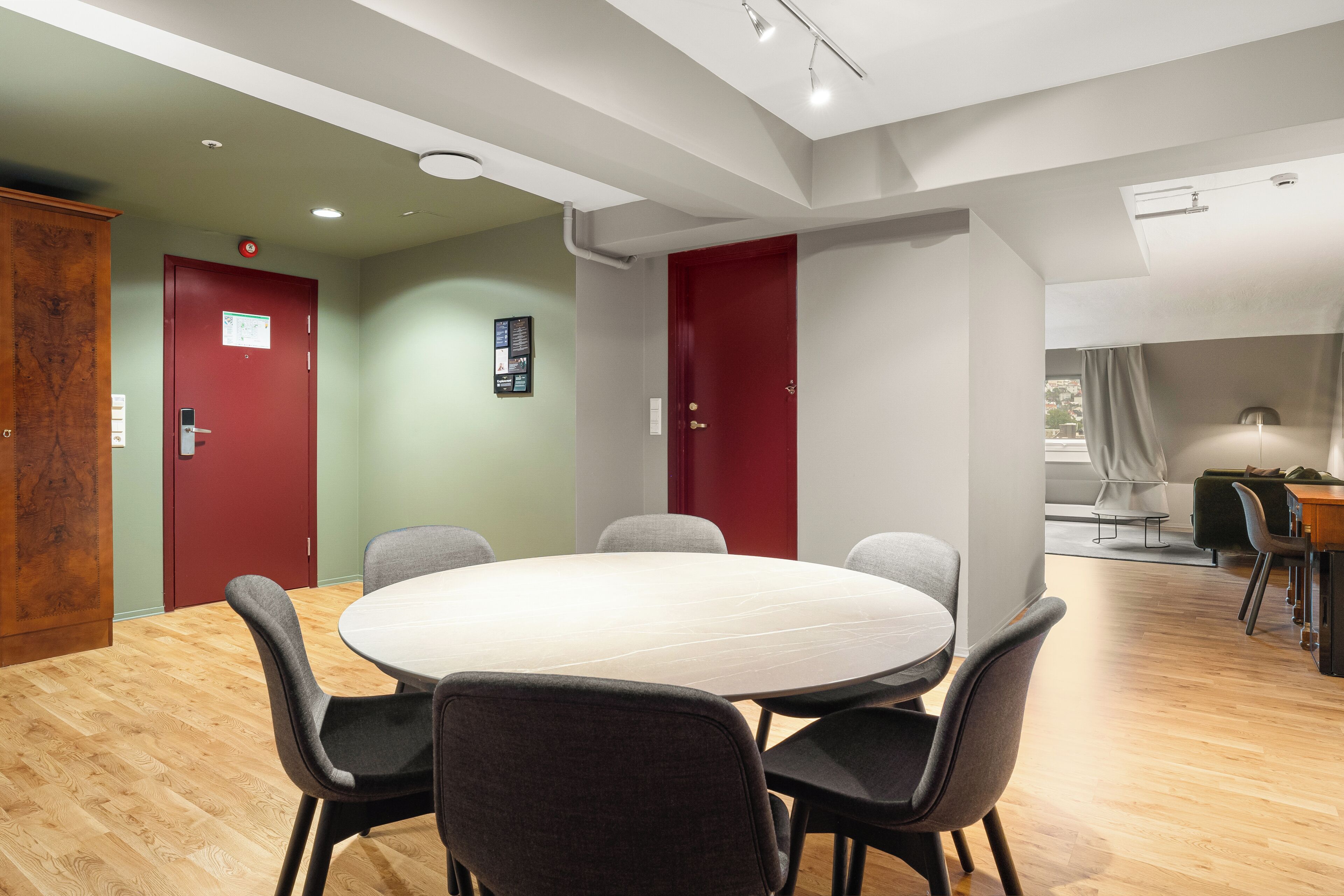 A conference room with a round table and chairs, wooden flooring, and a red door.