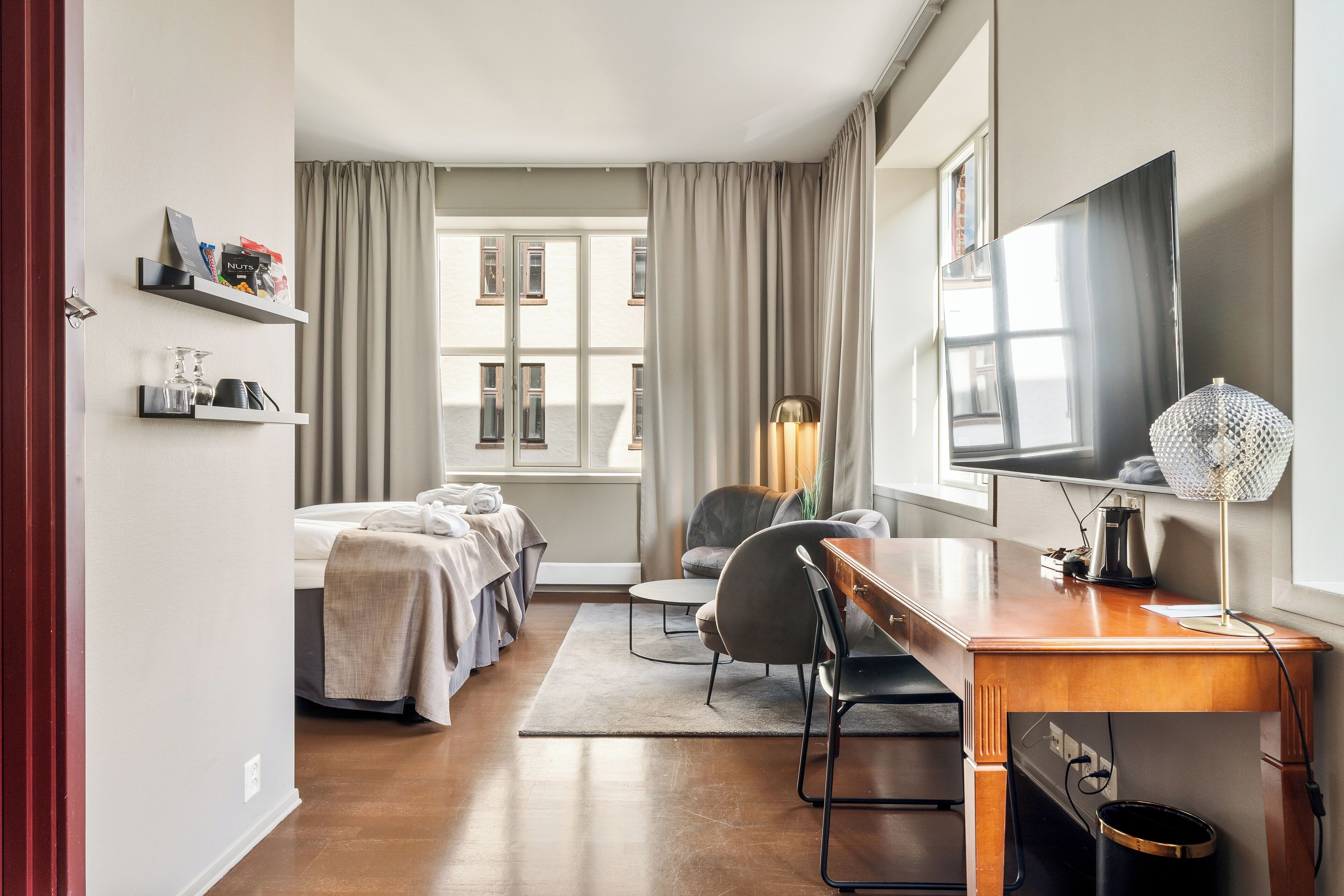 Een hotelkamer met een bed, een bureau, een stoel, een televisie en een raam met gordijnen.