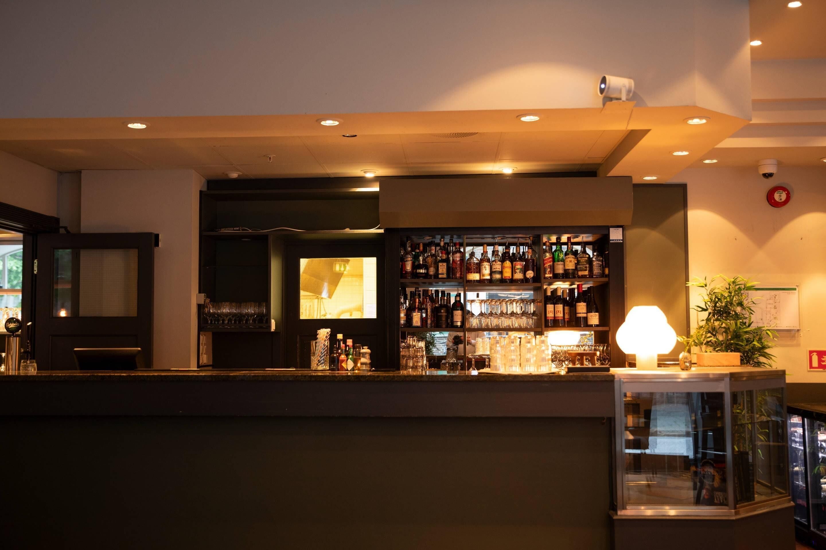 Un espace bar avec des étagères remplies de bouteilles, un comptoir et une lampe.
