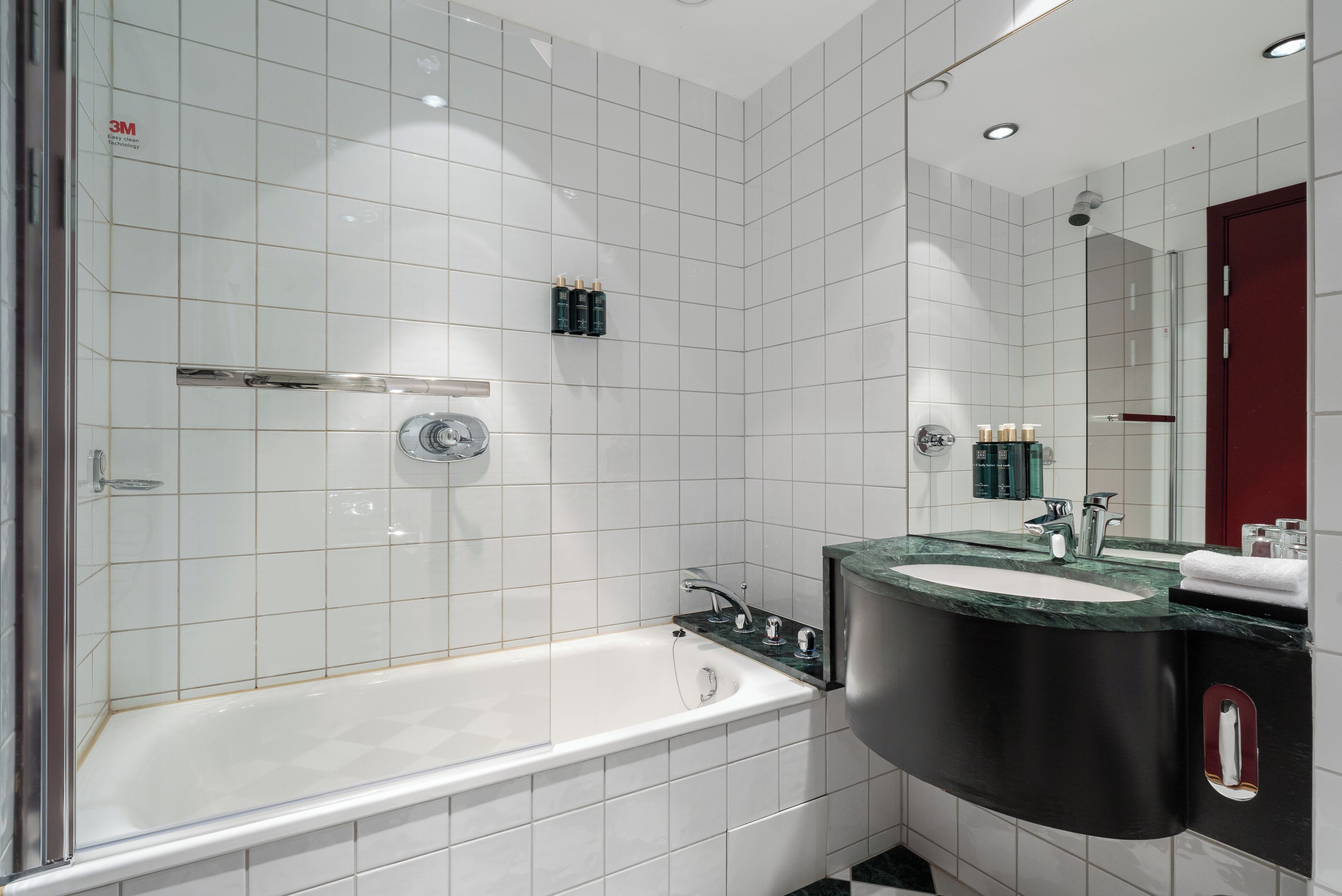 Een moderne badkamer met witte tegels, een badkuip, een wastafel met een zwart aanrechtblad en een spiegel.