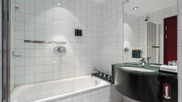 Een moderne badkamer met witte tegels, een badkuip, een wastafel met een zwart aanrechtblad en een spiegel.