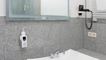A modern bathroom with a large mirror, white sink, granite countertop, and a towel rack.