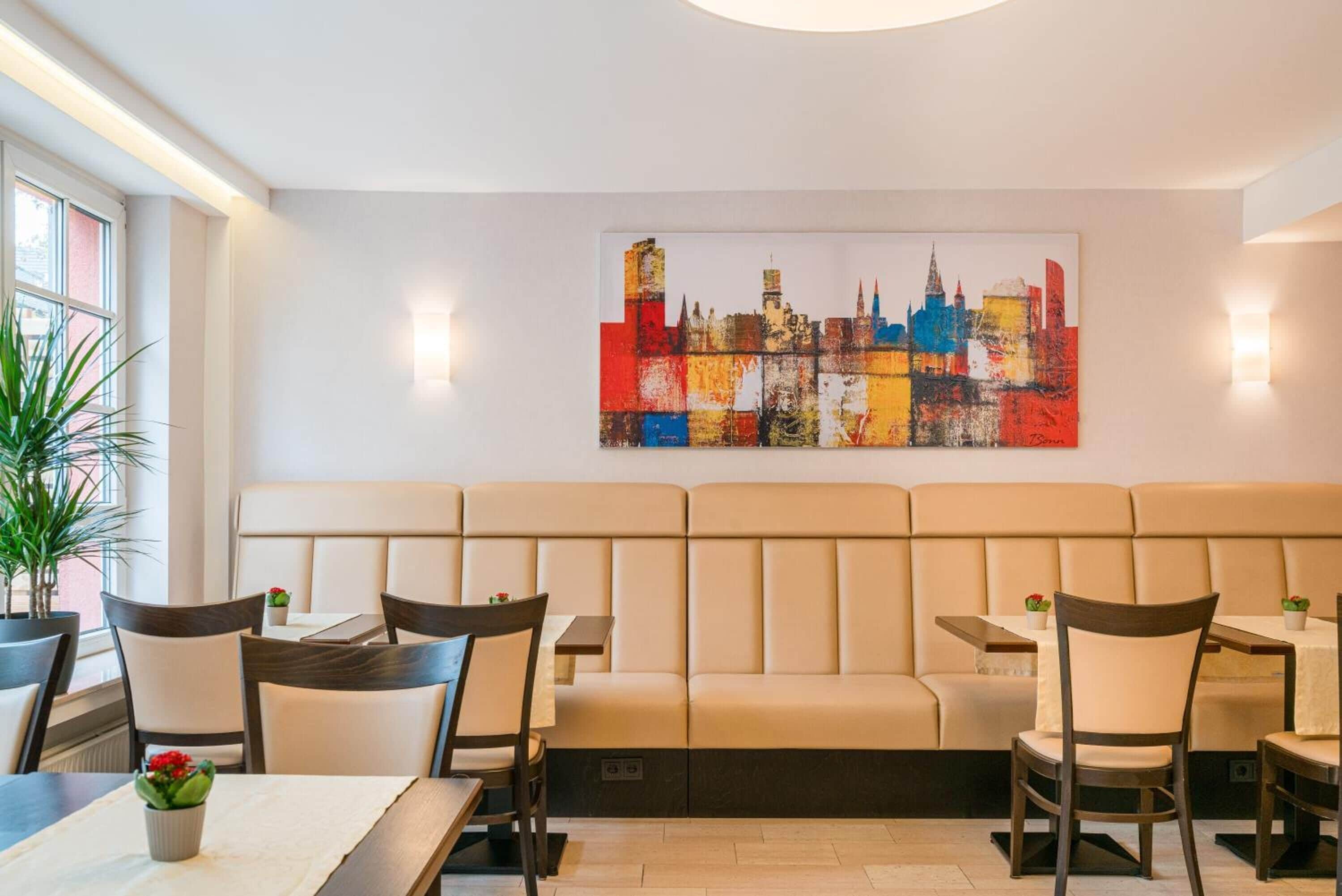 Un ristorante con una lunga area salotto con panche, tavoli, sedie e un'opera d'arte raffigurante un panorama urbano.