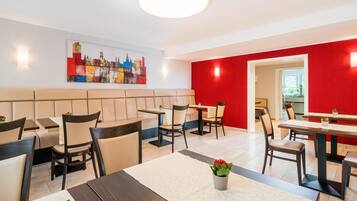 Un comedor de hotel moderno con cabinas y mesas, un cuadro de un paisaje urbano en la pared y una pared de acento roja.