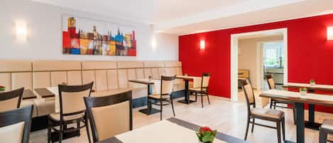 Un comedor de hotel moderno con cabinas y mesas, un cuadro de un paisaje urbano en la pared y una pared de acento roja.