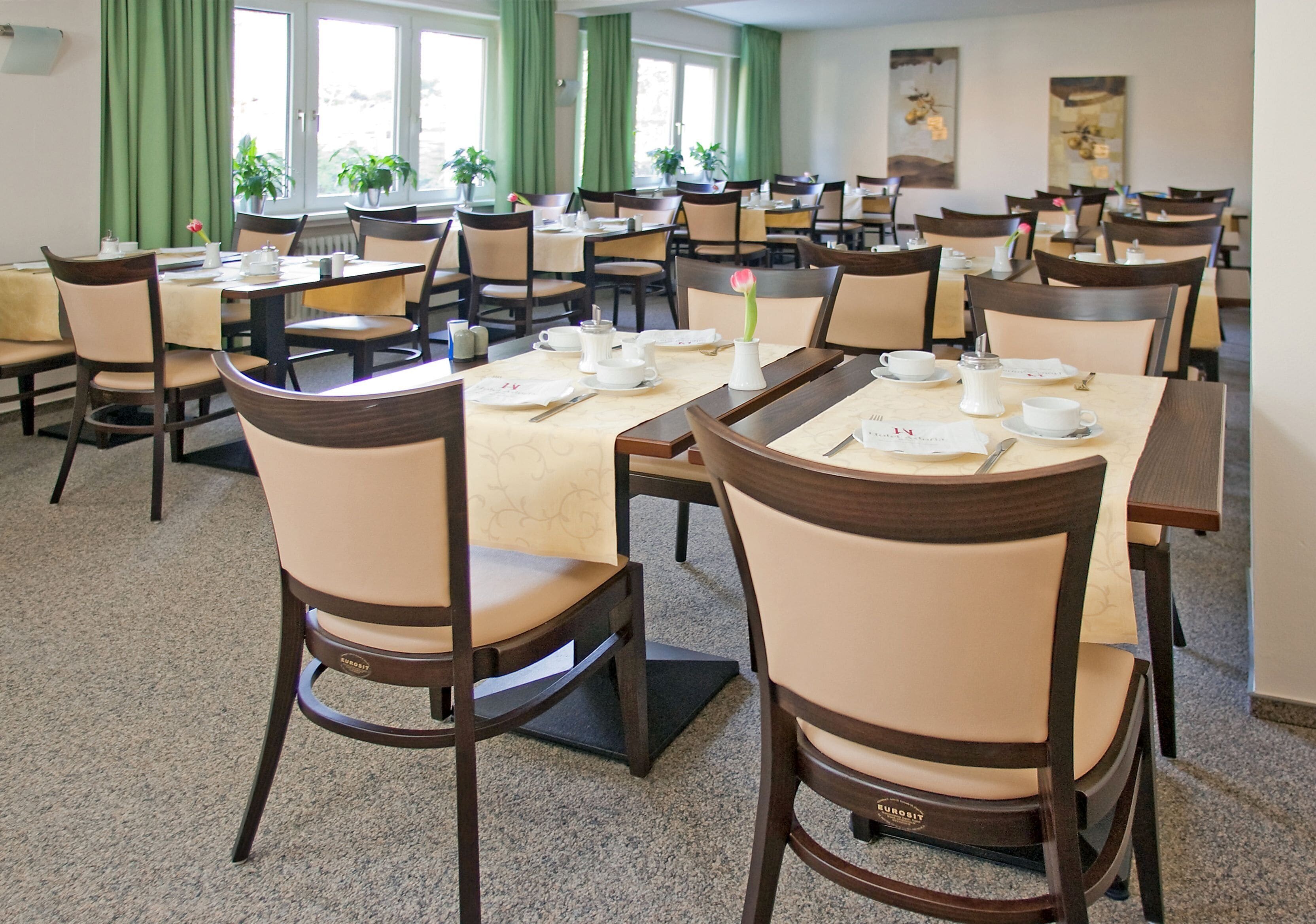 A hotel dining area with multiple tables and chairs, arranged in a spacious layout.