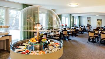 A buffet area with a glass dome centerpiece, various food items, and a seating area with tables and chairs.