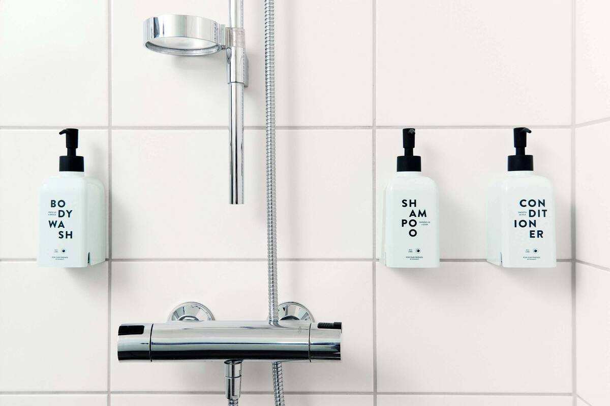Ein Badezimmer mit einer modernen Dusche, einem Duschkopf und drei Flaschen Badesiegel, Shampoo und Spülung an der Wand.