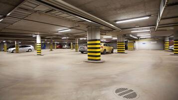 An underground parking garage with concrete pillars, fluorescent lighting, and several parked cars.