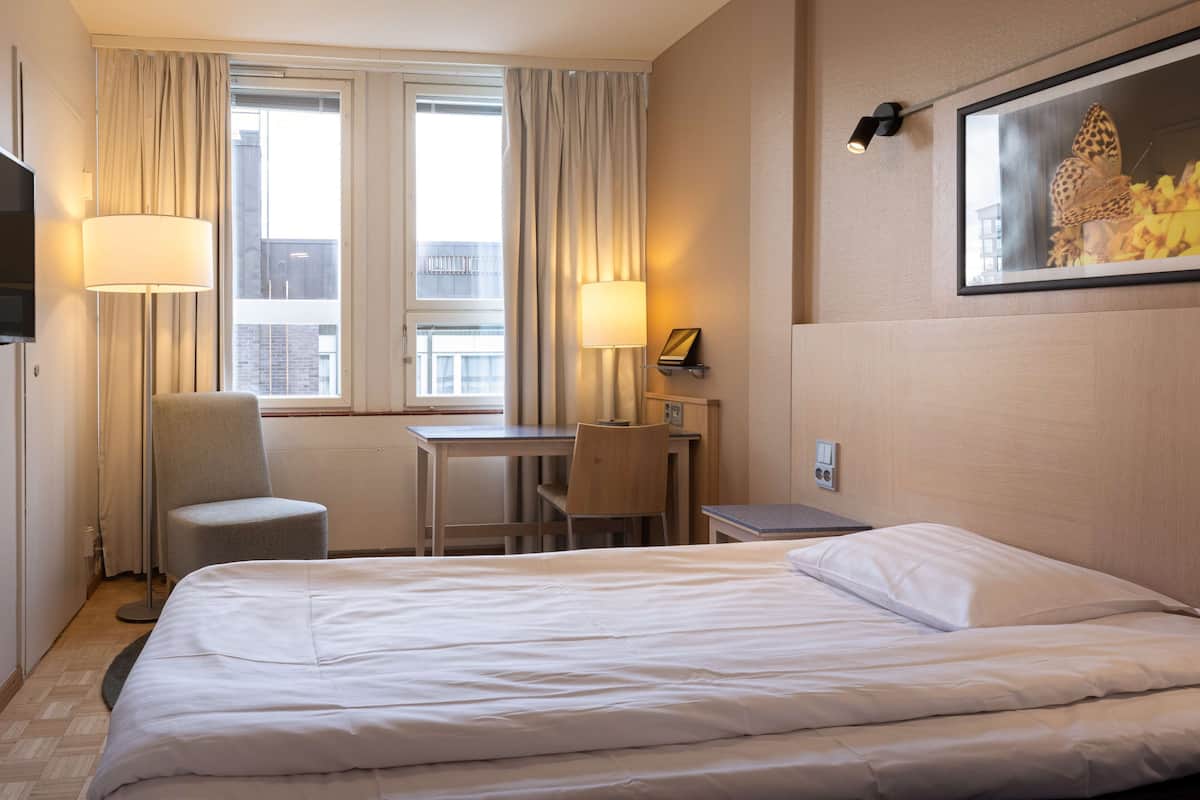 Hotellihuone, jossa on sänky, työpöytä, tuoli ja televisio.