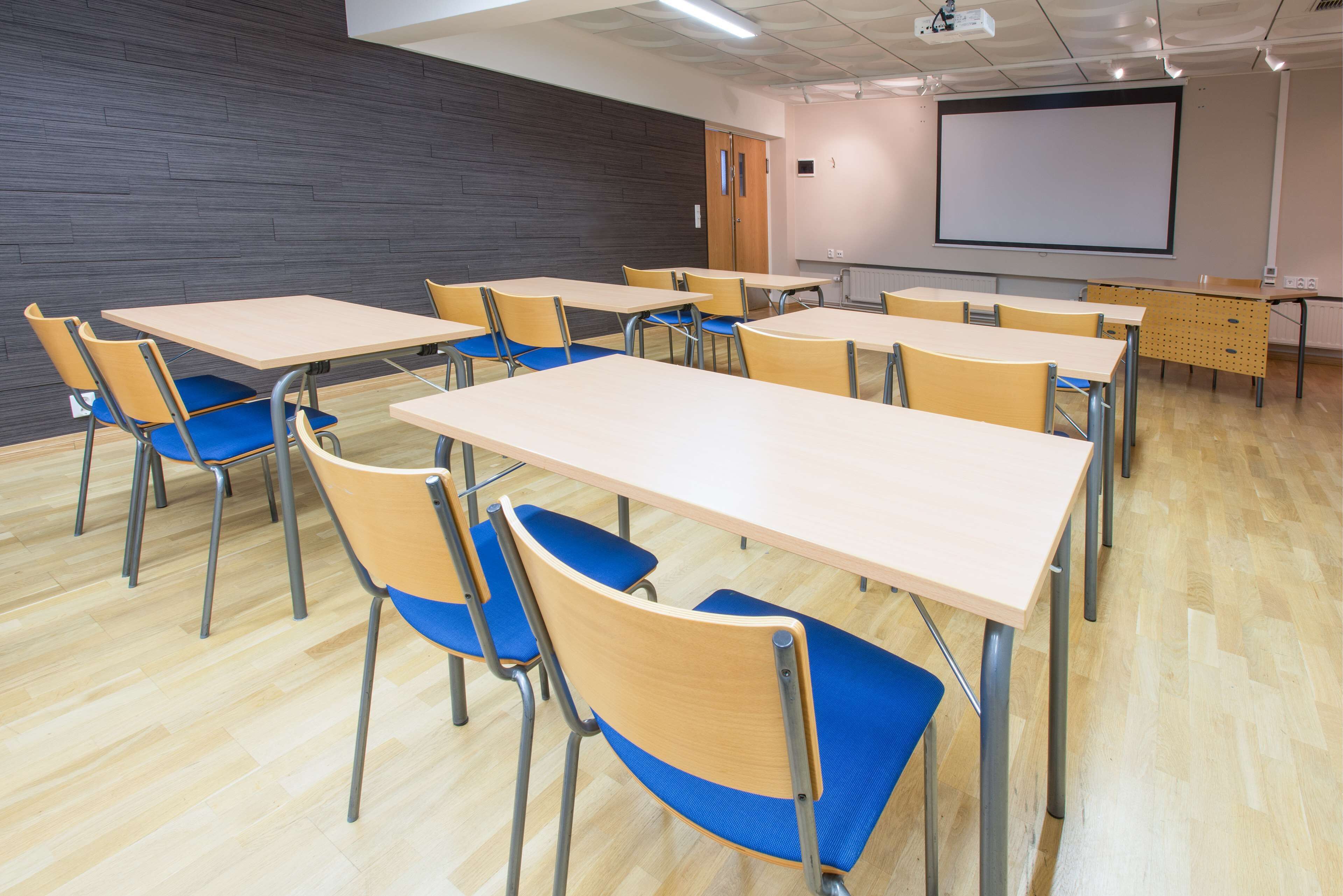 A classroom with wooden desks and blue chairs, a projector screen, and a whiteboard.
