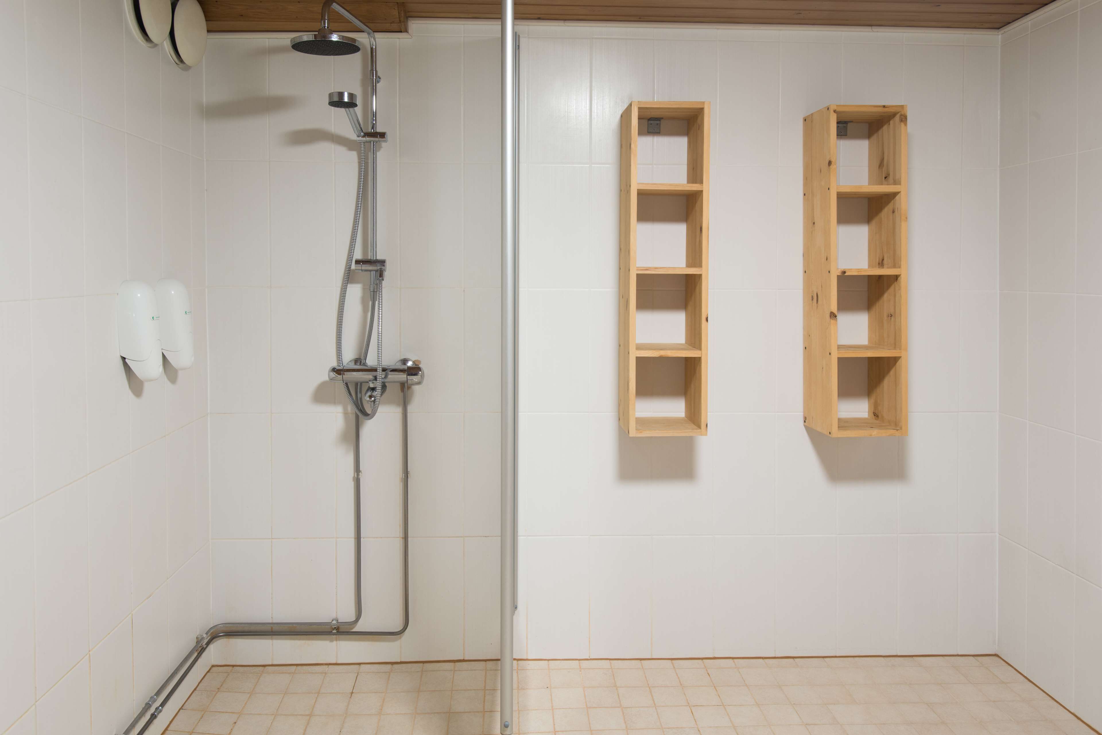 A shower with a handheld showerhead, a wall-mounted faucet, and a wooden shelf unit.