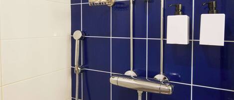 A bathroom with a blue tiled wall, a showerhead, a handheld shower, and two white dispensers.