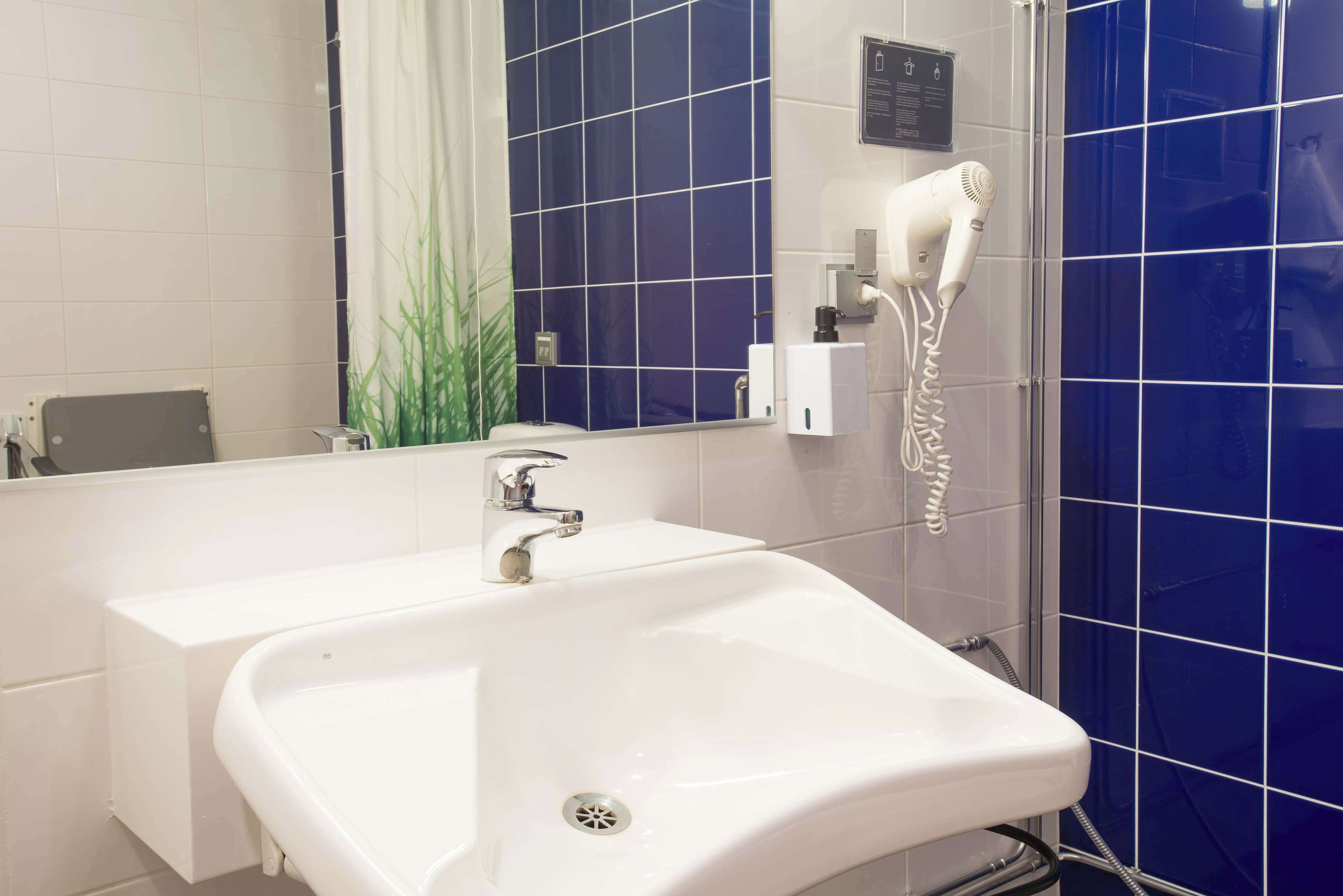 Un baño con lavamanos blanco, espejo, secador de pelo y paredes con azulejos azules.
