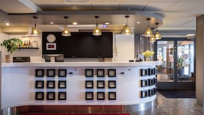 A hotel reception area with a curved counter, multiple pendant lights, a digital clock, and a red carpet.