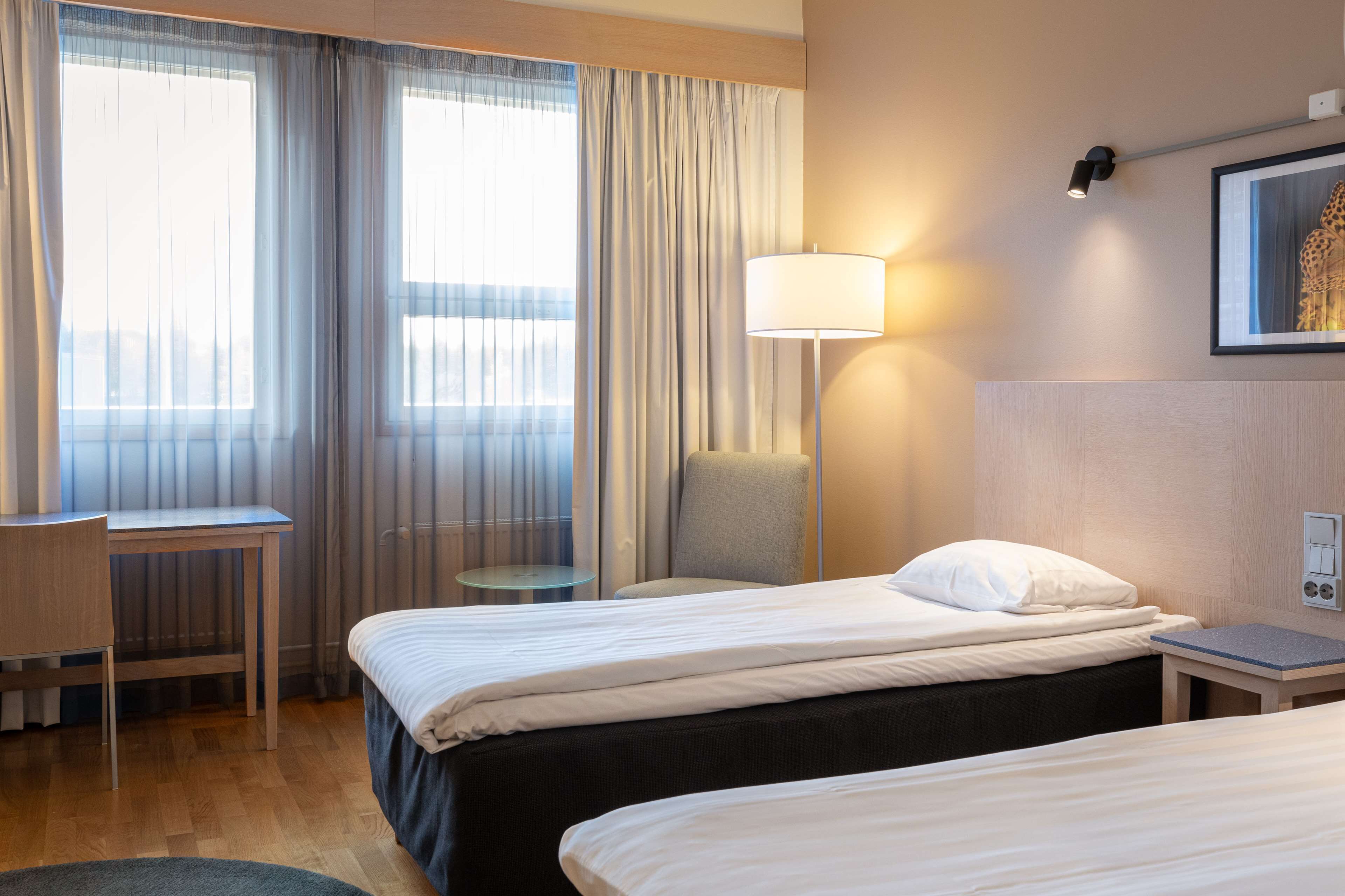 Habitación de hotel con dos camas, un escritorio, una silla, una lámpara y un cuadro en la pared.