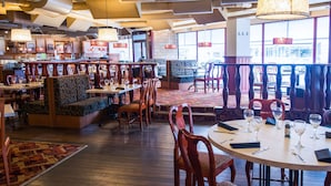 A restaurant interior with wooden flooring, cushioned seating, and tables set for dining.
