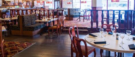A restaurant interior with wooden flooring, cushioned seating, and tables set for dining.