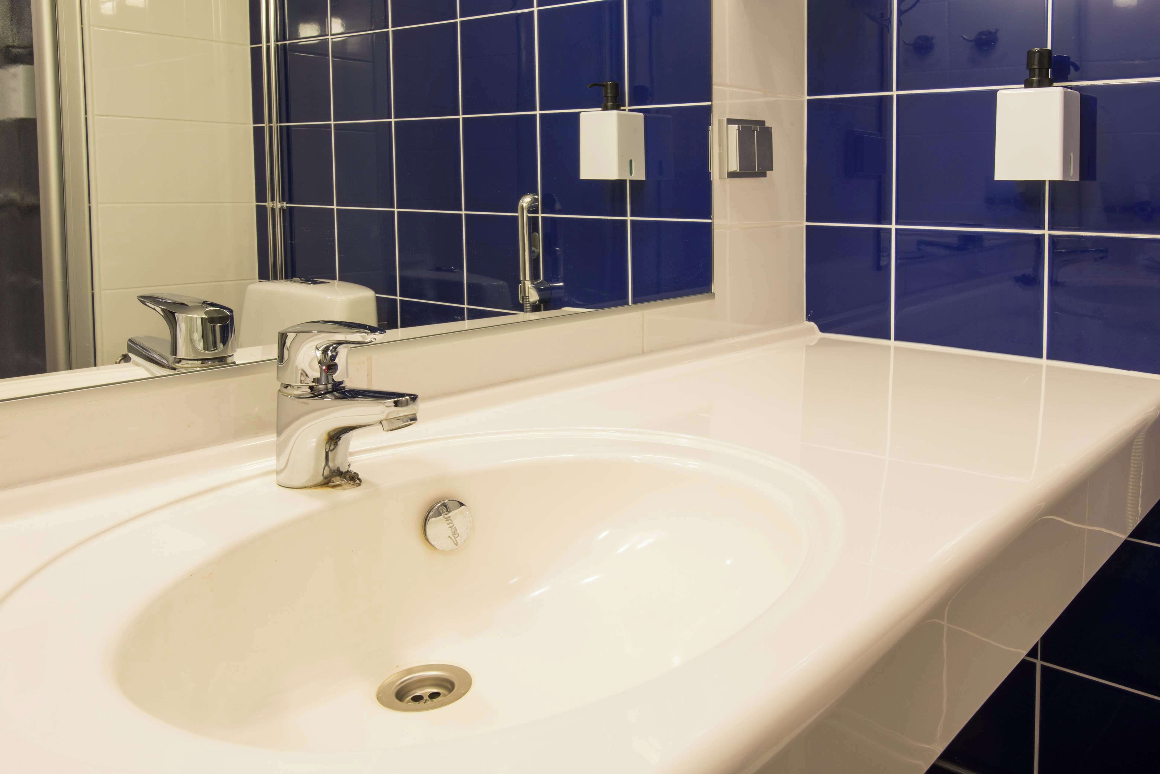 Un baño con lavamanos blanco, grifo cromado y espejo.