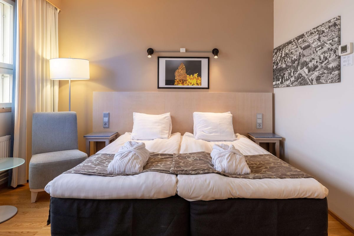 Hotellihuone, jossa on suuri sänky, kaksi yöpöytää, tuoli, lamppu ja seinällä oleva kehystetty kuva.
