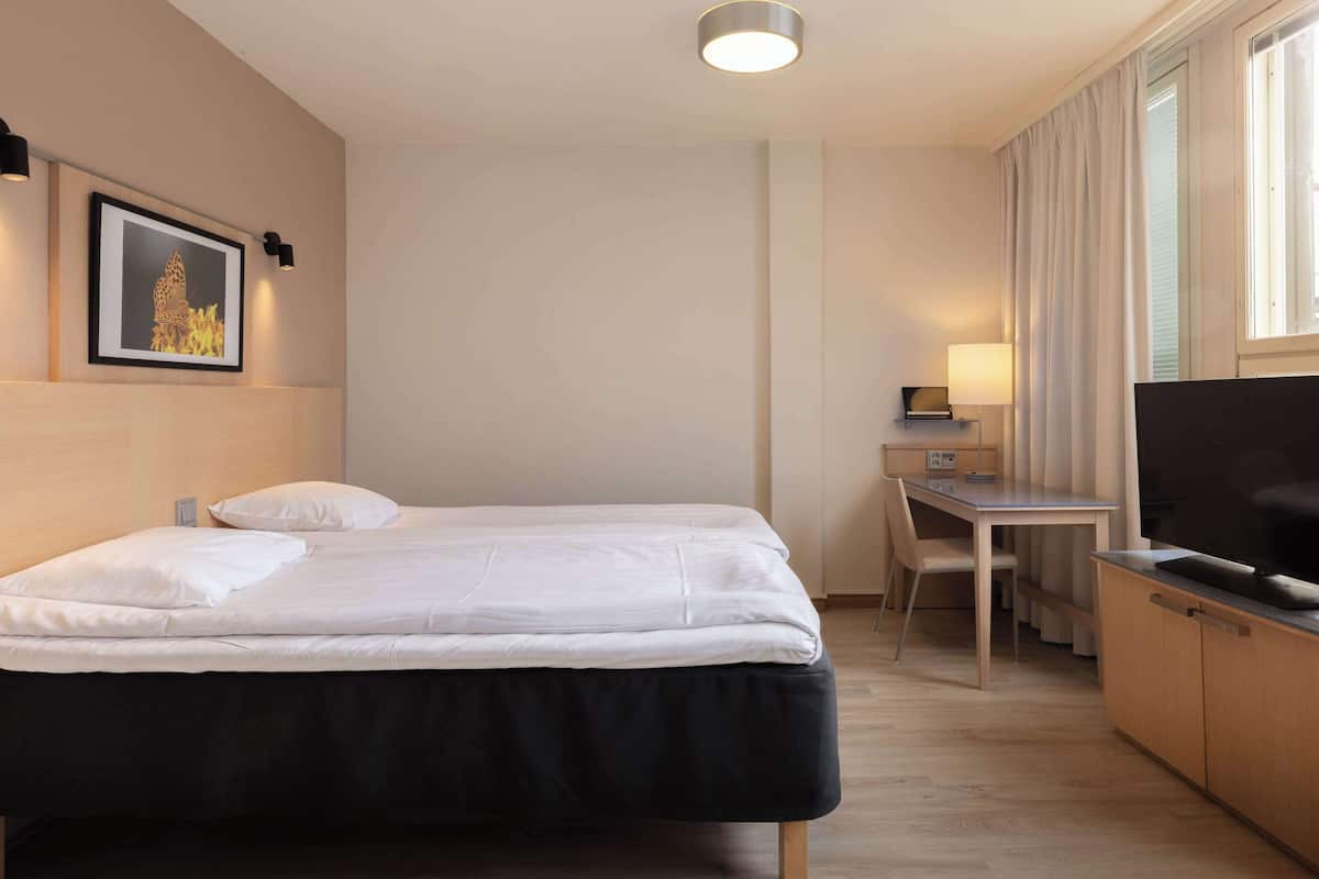 Hotellihuone, jossa on sänky, työpöytä, televisio ja taulu seinällä.