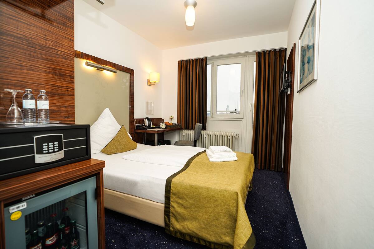 A hotel room with a bed, a desk, a minibar, and a window with curtains.