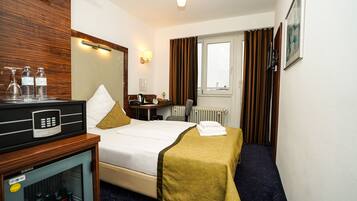 Una habitación de hotel con cama, escritorio, minibar y ventana con cortinas.