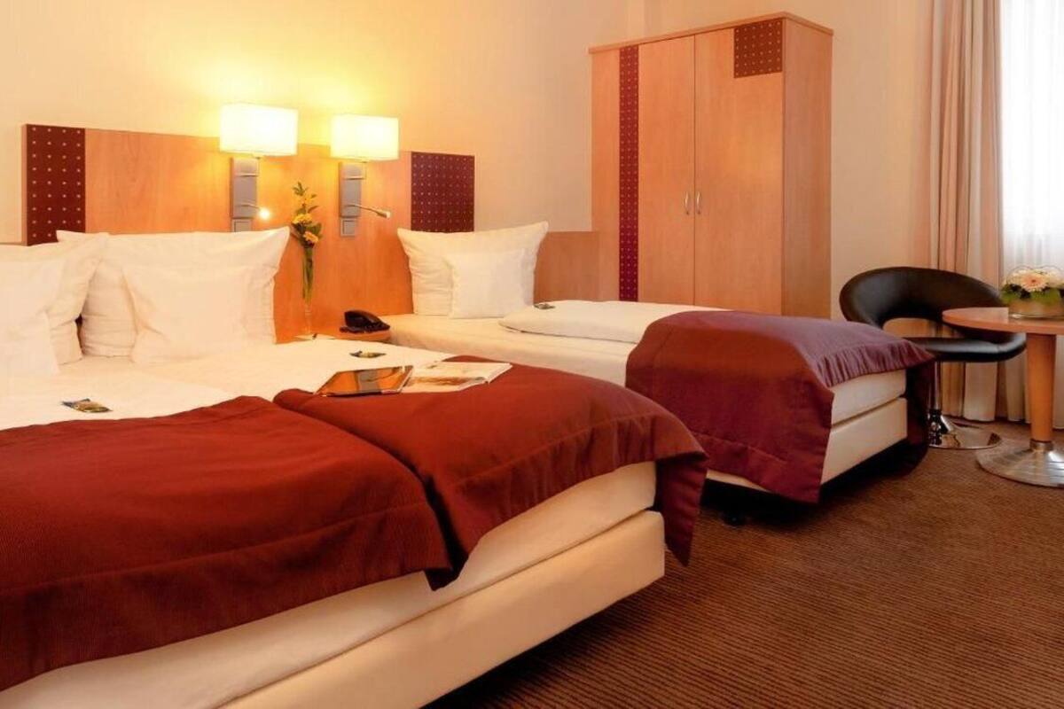 A hotel room with two beds, a desk, a chair, and a wardrobe.