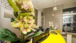 A reception desk with a yellow accent, a potted plant, and a clock.