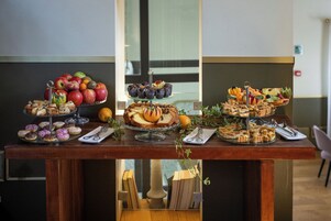 A buffet table with various food items including fruits, pastries, and sandwiches.