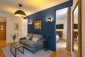 Een moderne woonkamer met een grijze bank, een klein bijzettafeltje en een decoratieve vaas. Er zijn wandlampen en een grote spiegel.