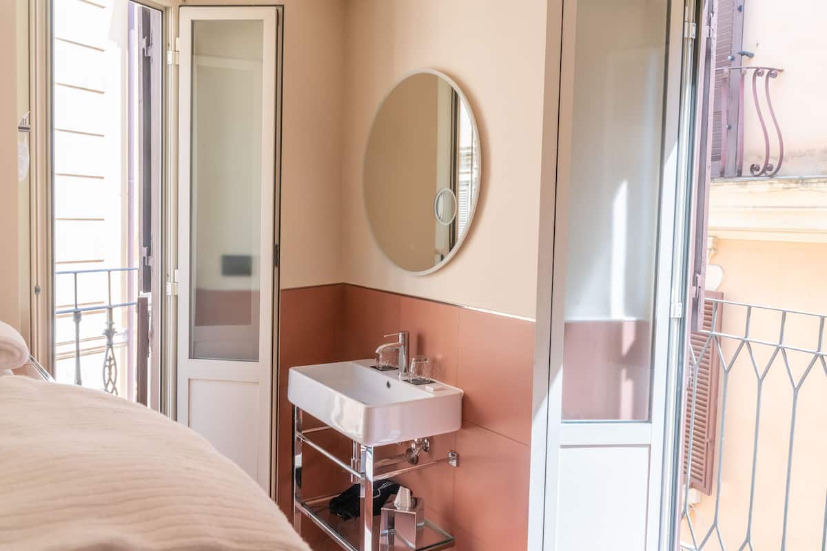 Une chambre d’hôtel avec un lit, une salle de bain dotée d’un lavabo et d’un miroir, et un balcon avec une rambarde en métal.