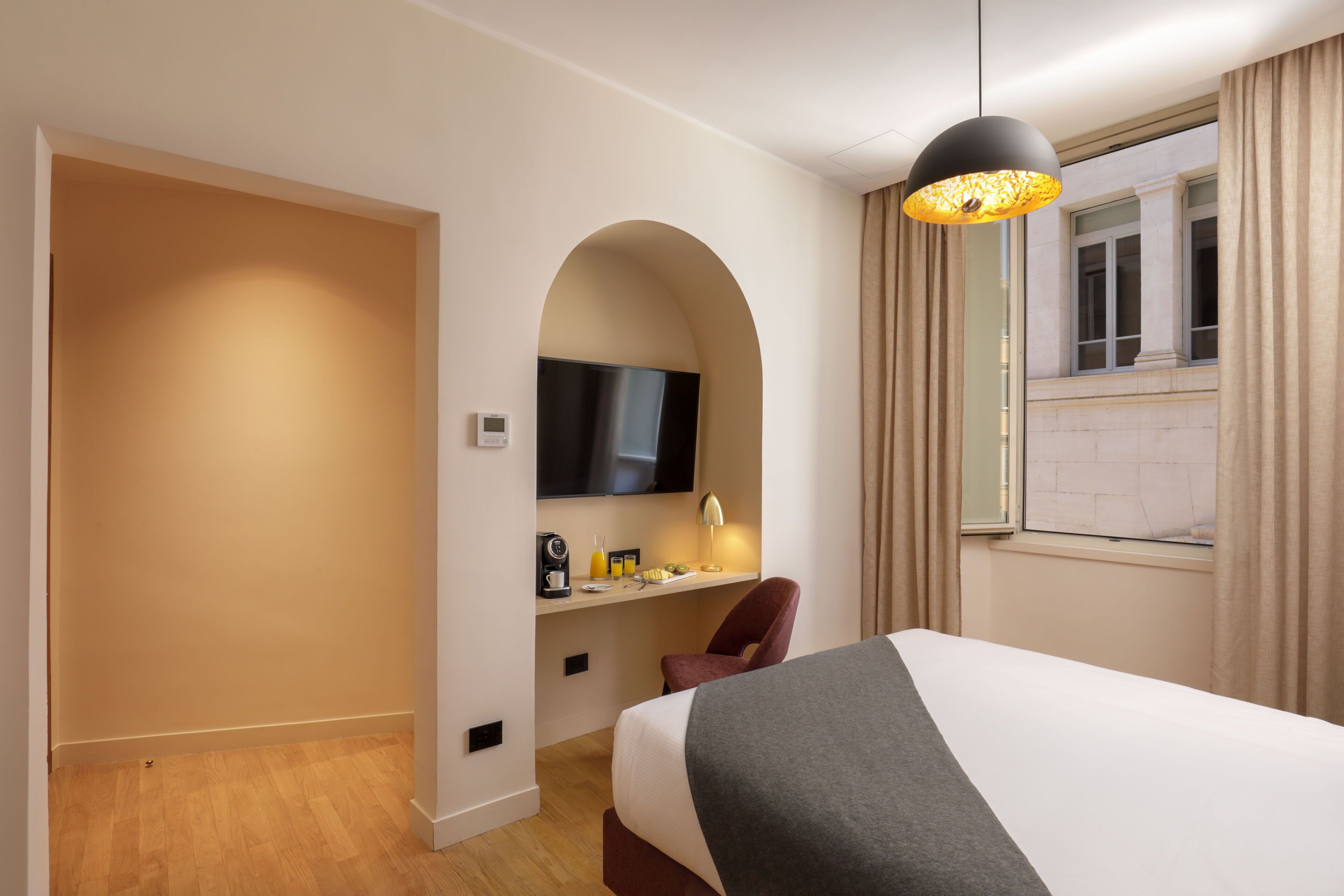 Una camera d'albergo con un letto grande, una scrivania con TV a schermo piatto, una macchina del caffè e una finestra con tende.