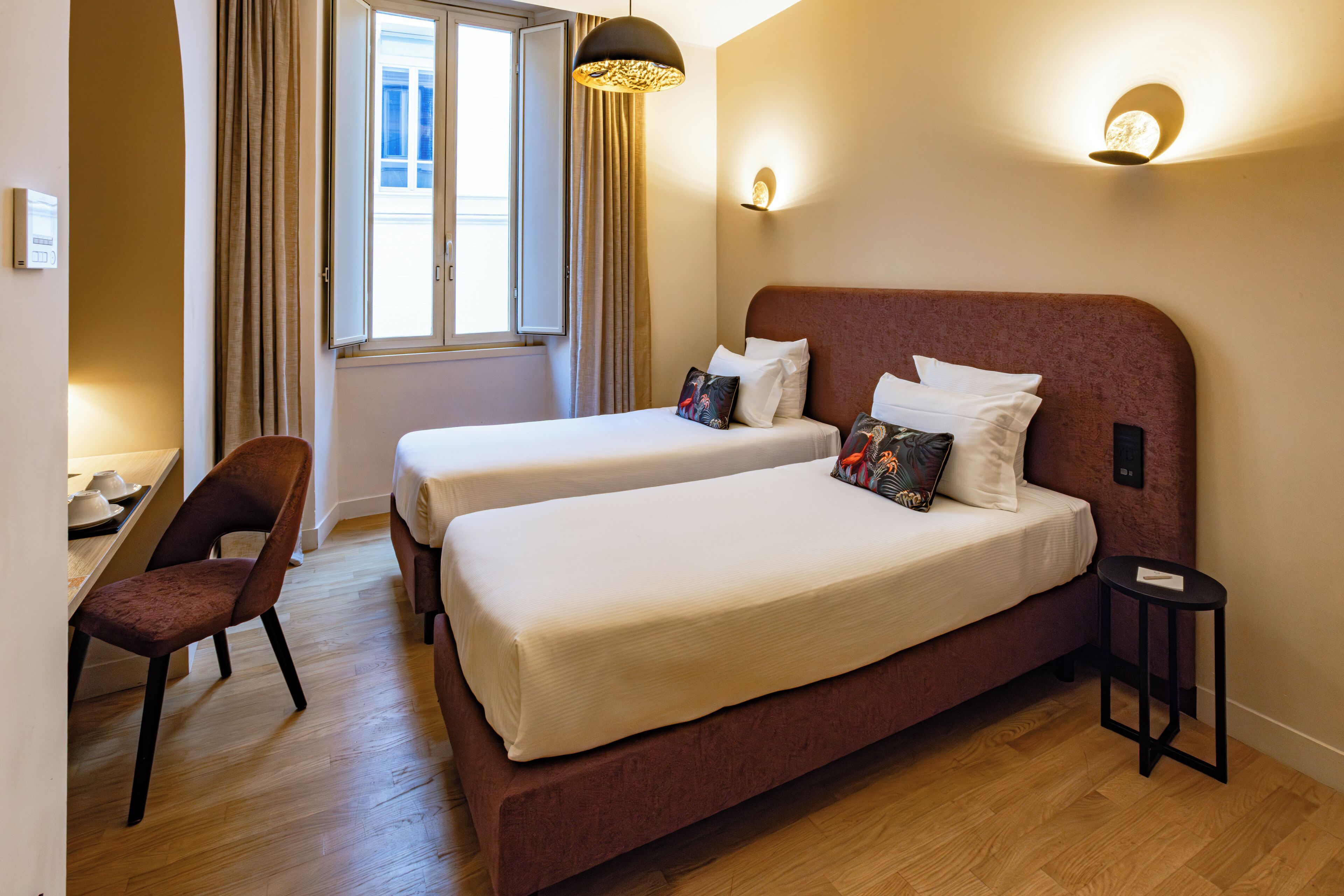 Een hotelkamer met twee bedden, een stoel, een tafeltje en een raam met gordijnen.