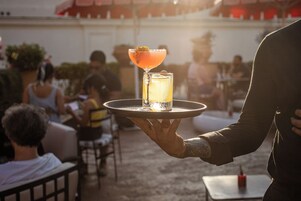 A person holding a tray with a cocktail and a glass of water.