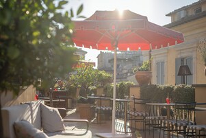 An outdoor seating area with tables and chairs, a red umbrella, and potted plants.