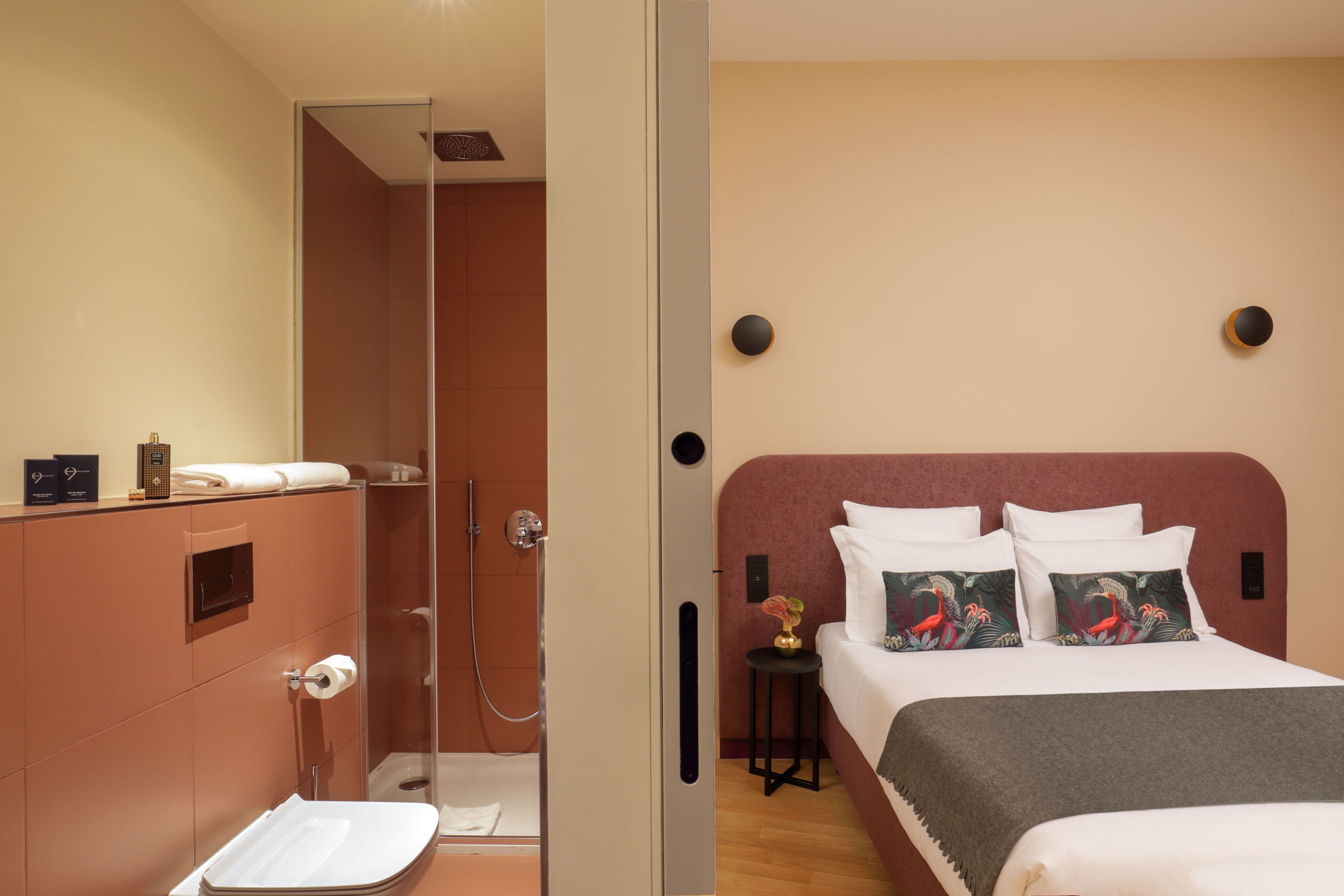 A modern hotel room with a shower, toilet, and a bed with decorative pillows.
