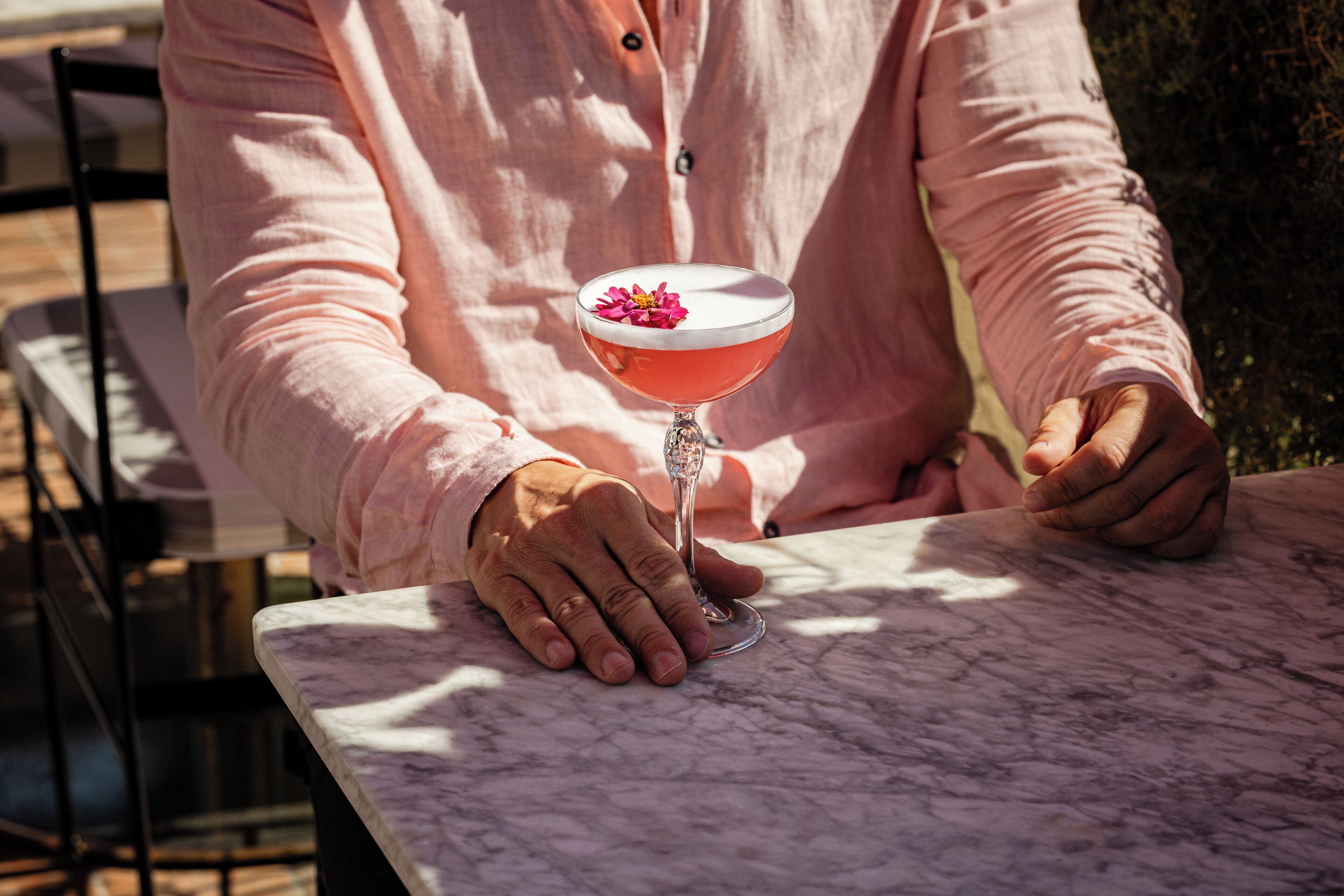 A person sitting at a marble table with a cocktail in a glass.