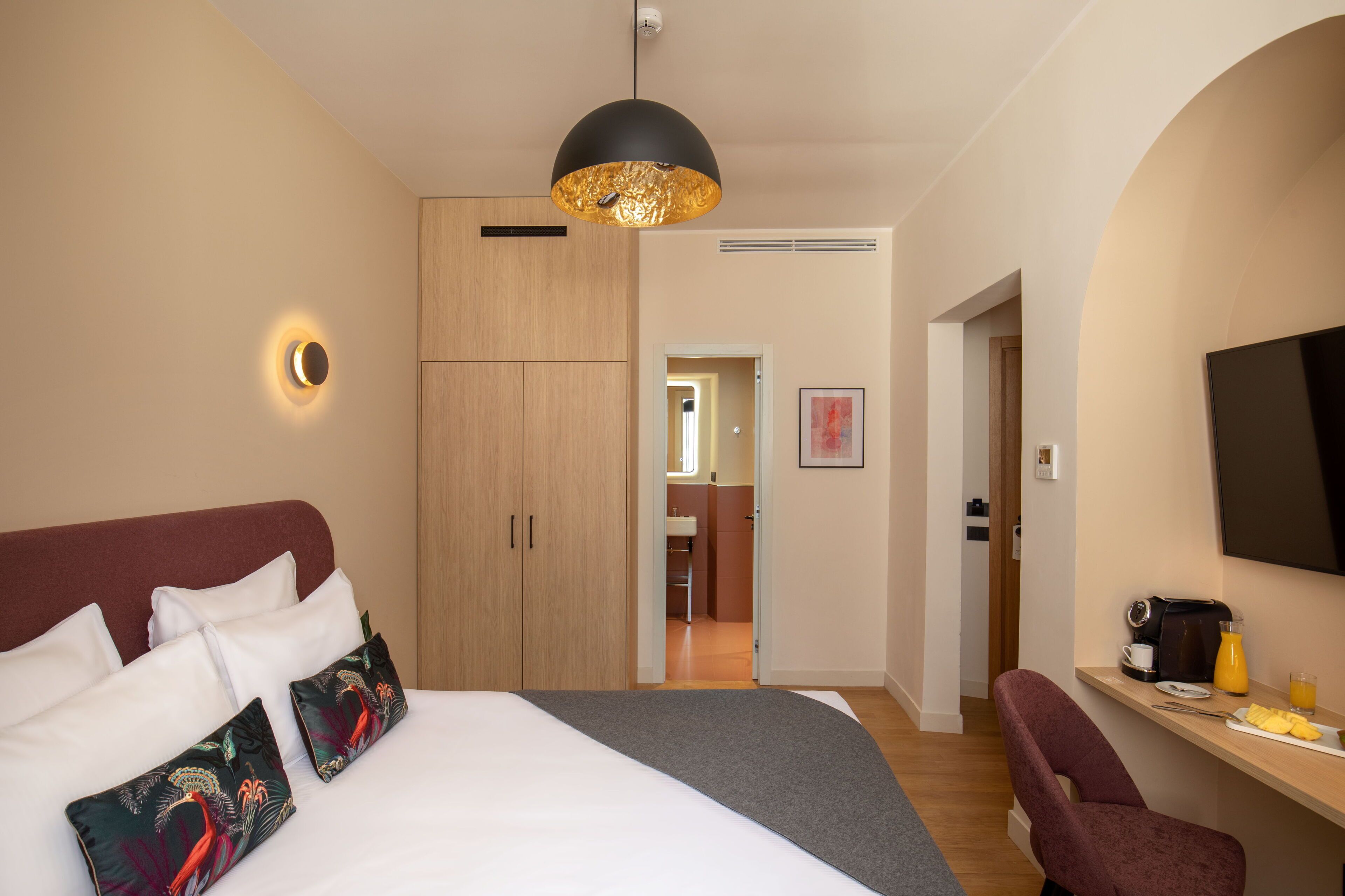 A modern hotel room with a large bed, a desk with a chair, a flat-screen TV, and a bathroom visible through an open door.