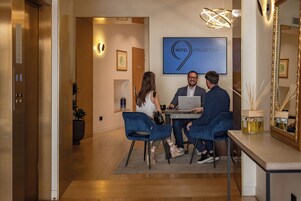 En hotellobby med en reception, et stort indramet skilt med teksten "HOTEL COLLECTION" og en moderne lysekrone.