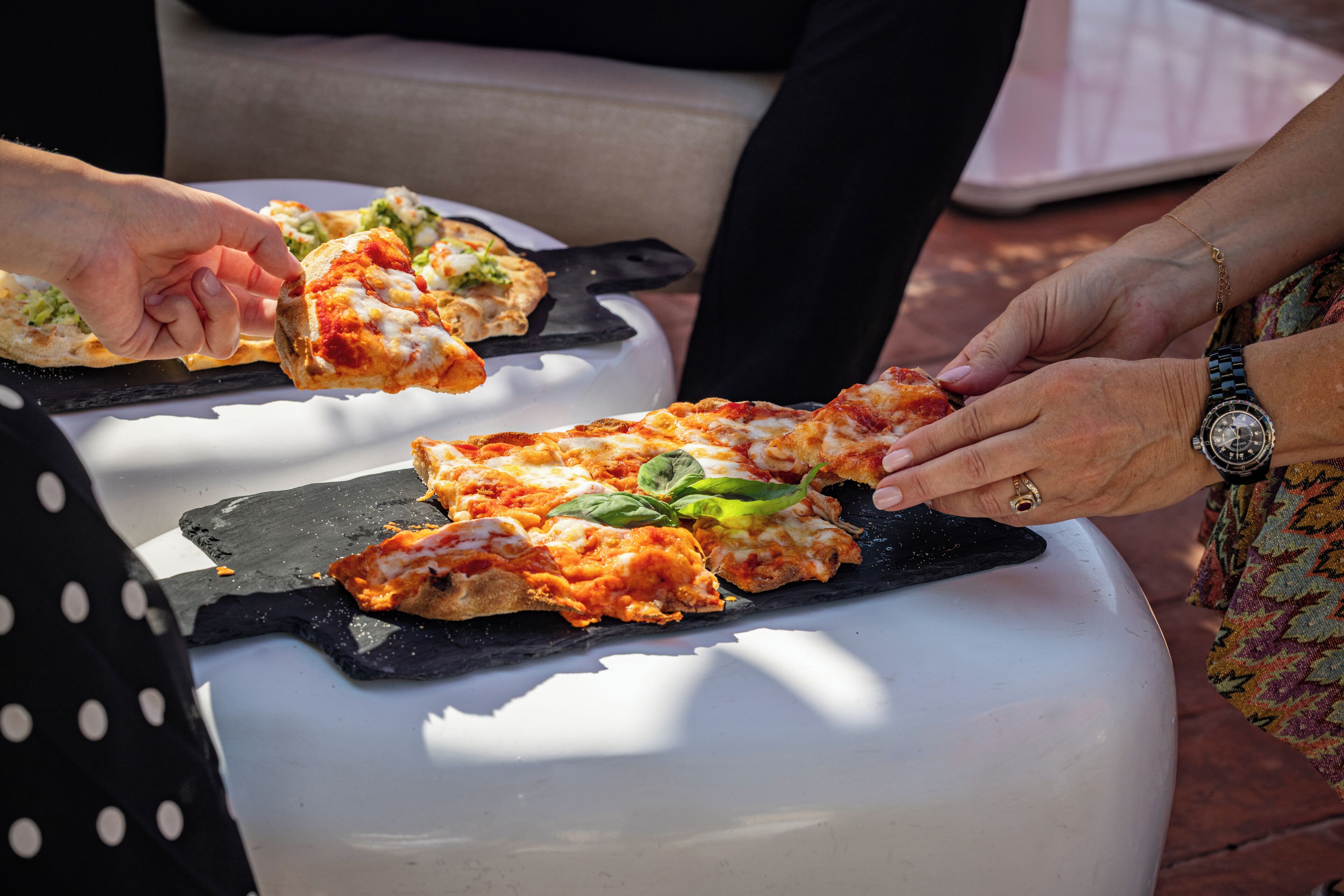 A person holding a slice of pizza with toppings, placed on a white surface.