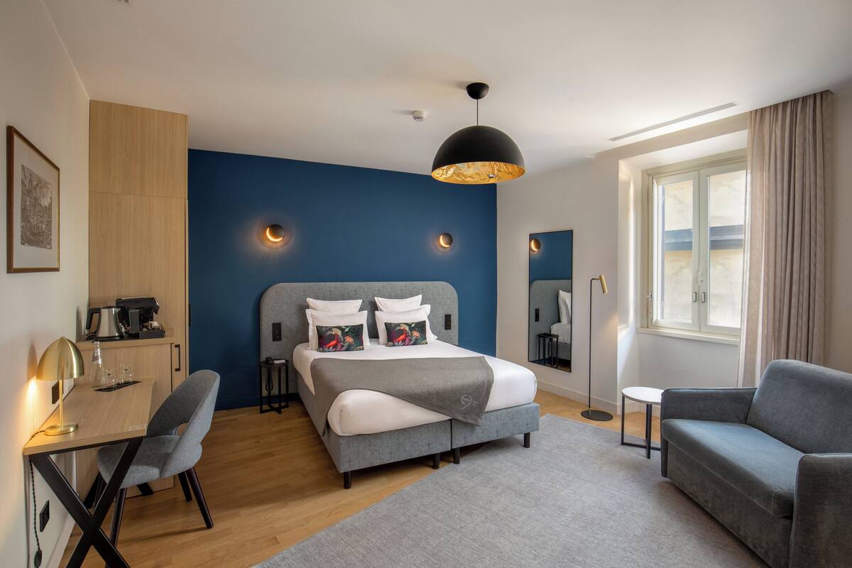 Une chambre d’hôtel moderne équipée d’un lit, d’un bureau, d’une chaise et d’une grande fenêtre.