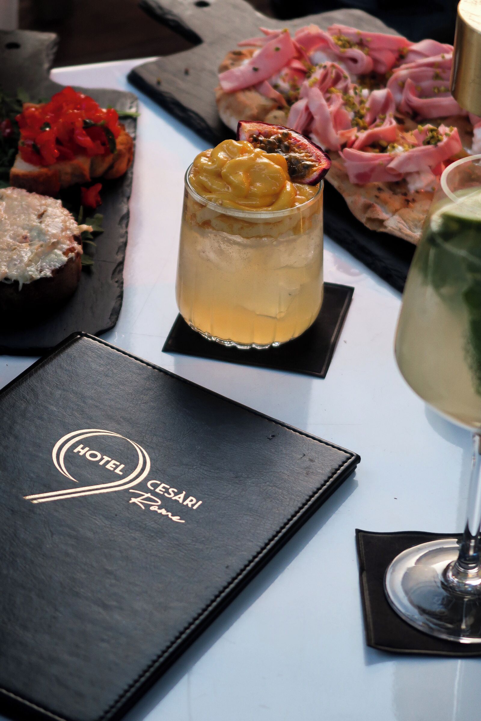 A hotel menu, a glass of yellow drink, and a plate of food including a stuffed pepper and a slice of pizza.