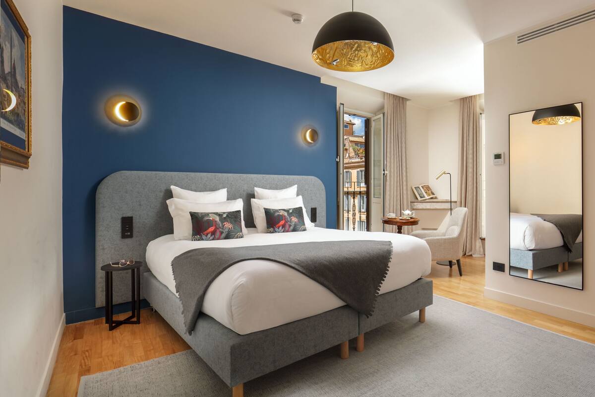 Une chambre à coucher moderne avec un grand lit, une table de chevet, une chaise, un miroir et une vue sur l’extérieur.