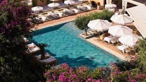 A pool area with lounge chairs and umbrellas, surrounded by lush greenery and flowers. - The Margi (Vari-Voula-Vouliagmeni)