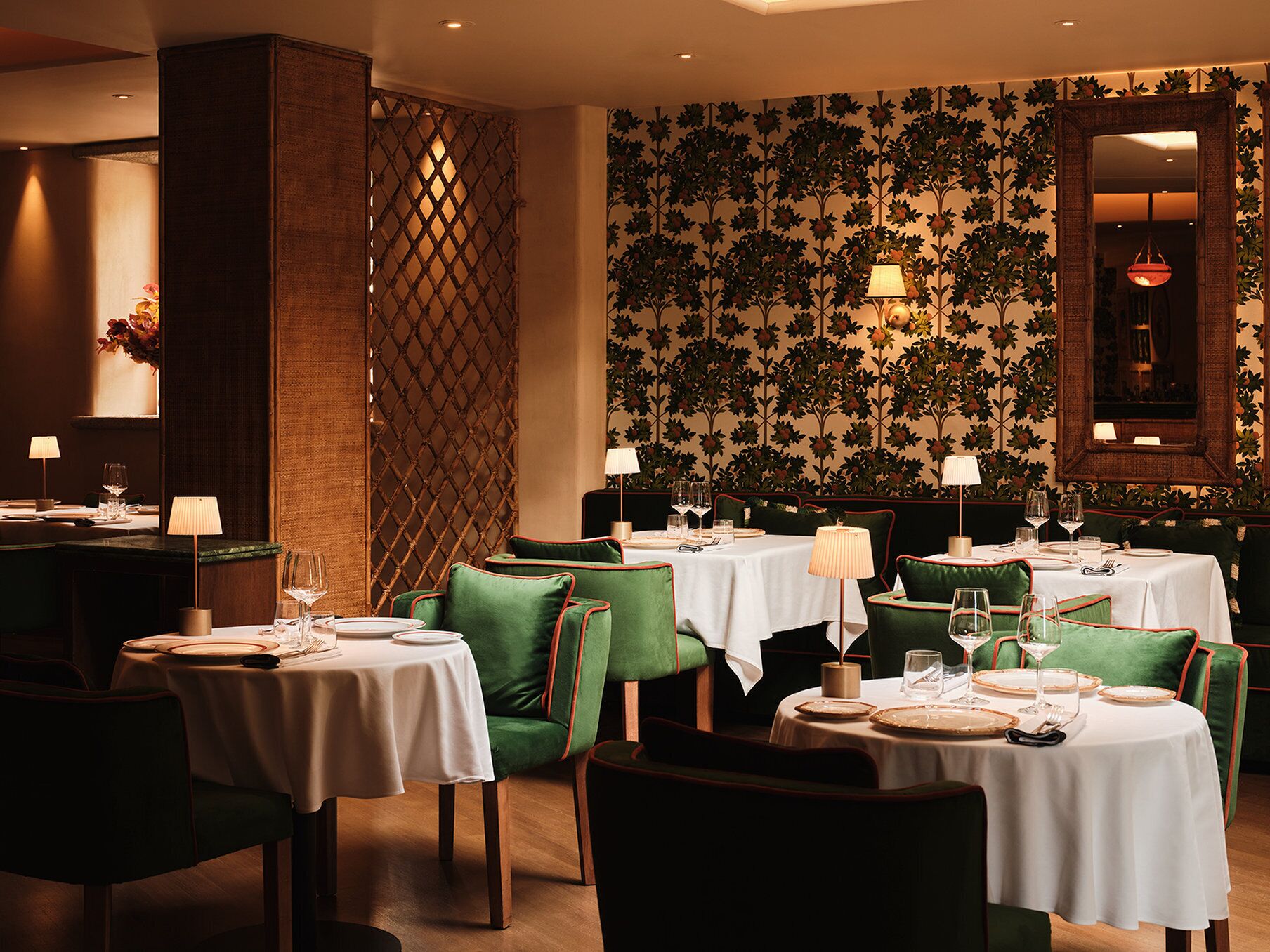 A restaurant with round tables, green upholstered chairs, and a floral wallpaper design.