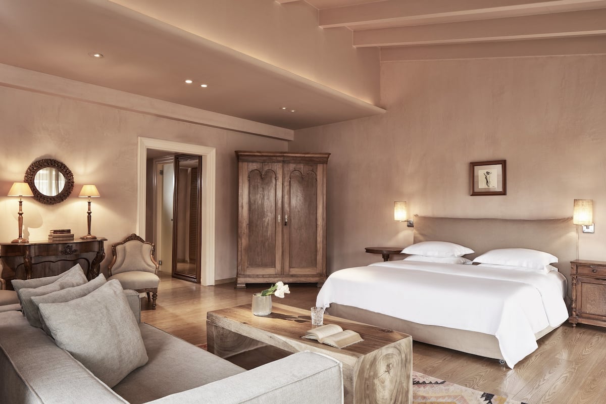A bedroom with a bed, a sofa, a wooden coffee table, a wardrobe, and a mirror.