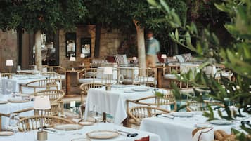 Un área de comedor al aire libre con mobiliario de mimbre y manteles blancos.