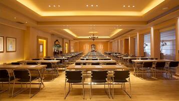 A conference room with multiple tables and chairs, a chandelier, and framed artwork on the walls.